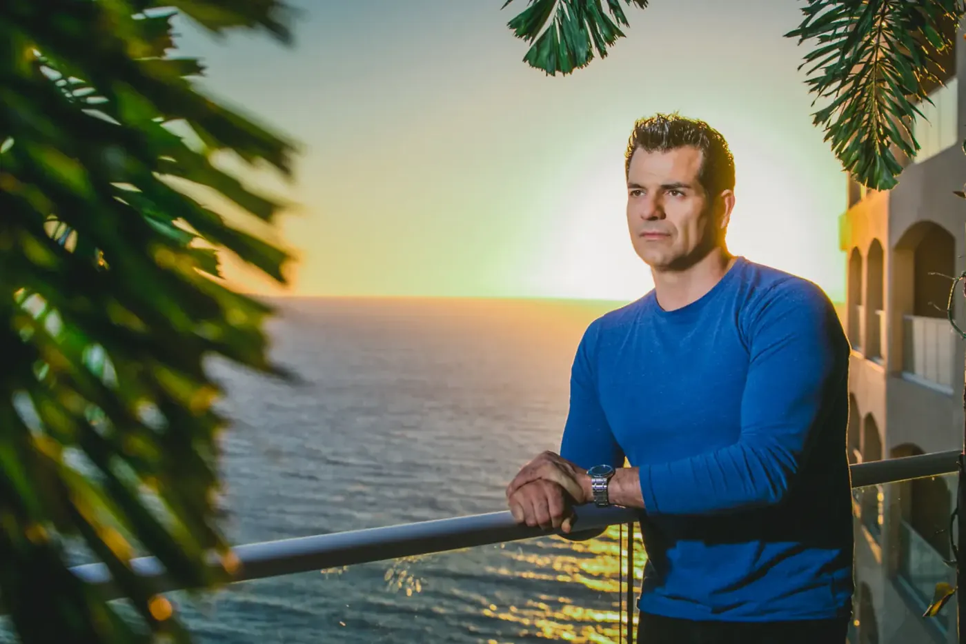 Johnny Tabaie, founder, standing at an oceanfront balcony at sunset